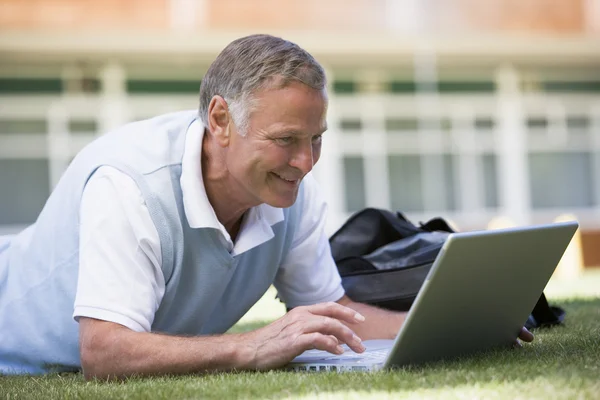 Mann benutzt Laptop während er im Gras auf dem Campus liegt — Stockfoto