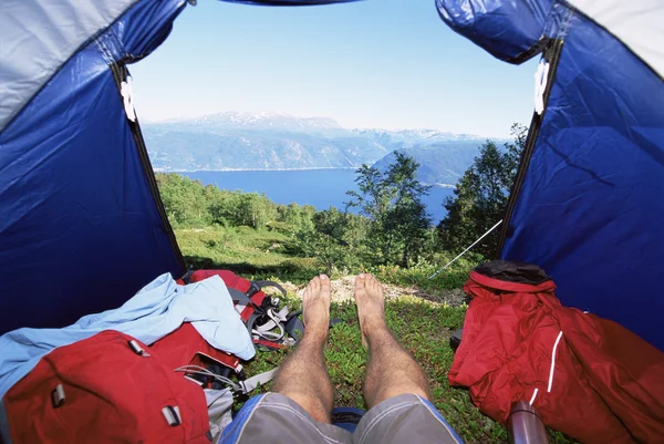 Homem deitado na tenda com vista para o lago — Fotografia de Stock