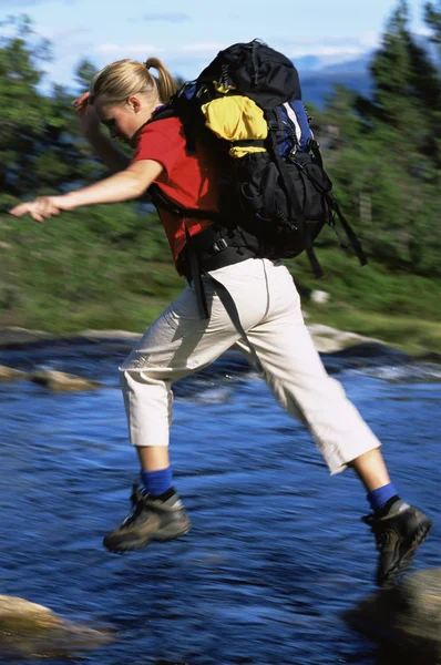 徒步旅行者在穿越河流时跳跃于岩石 — 图库照片