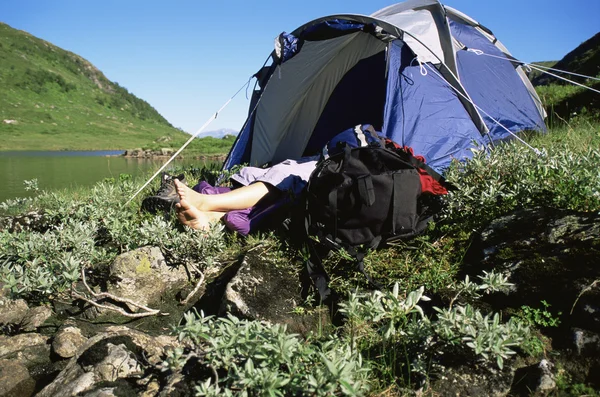 Camper relaxing at water's edge by tent — Stock Photo, Image