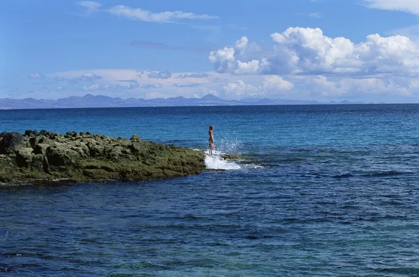 Jovem mulher de pé sobre rochas, olhando para o mar — Fotografia de Stock