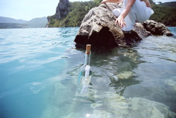 Mujer buscando un mensaje en una botella flotando en el mar — Foto de Stock