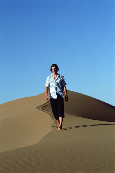 Молодой человек идет по песчаной дюне — стоковое фото