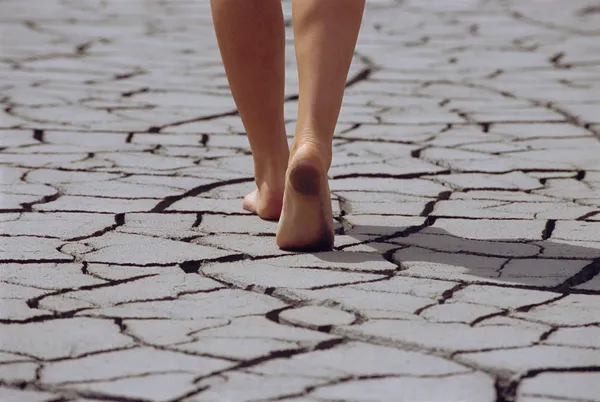 Woman walking barefoot across cracked earth, low section — Stock Photo, Image