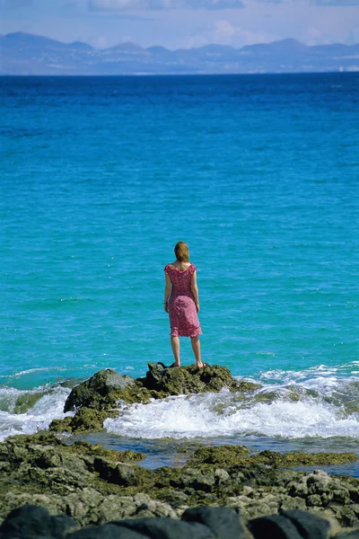 Jeune femme debout rochers, regardant vers la mer — Photo
