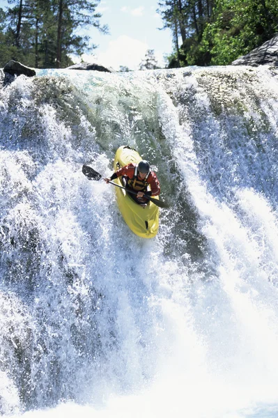 Молодой человек спускается на каяке по водопаду — стоковое фото