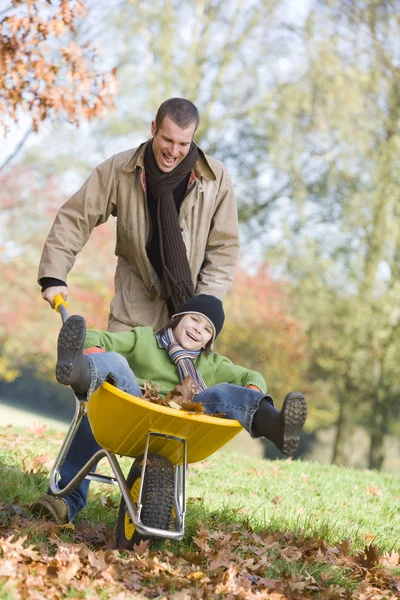 父亲给儿子骑在通过秋天的树叶 Wheelbarrowe — 图库照片