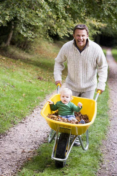 父亲给年幼的儿子骑独轮车沿秋路径中 — 图库照片