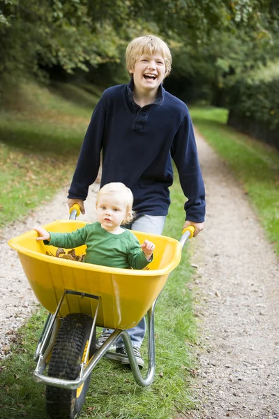Boy pushing toddler in wheelbarrow — Stock Photo, Image