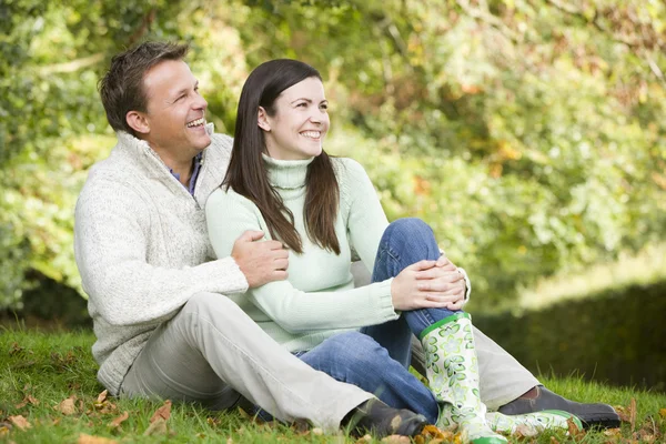 坐在秋天的树林草地上的年轻夫妇 — 图库照片