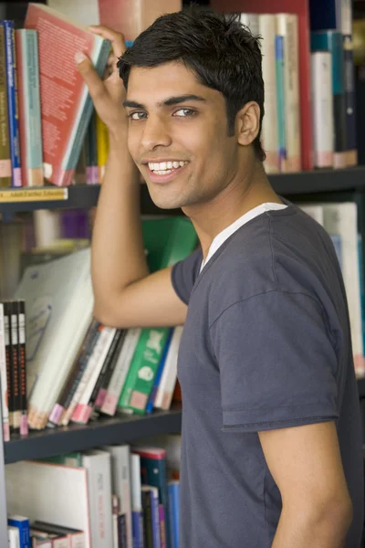 Male college student reaching for a library book — Stock Photo, Image