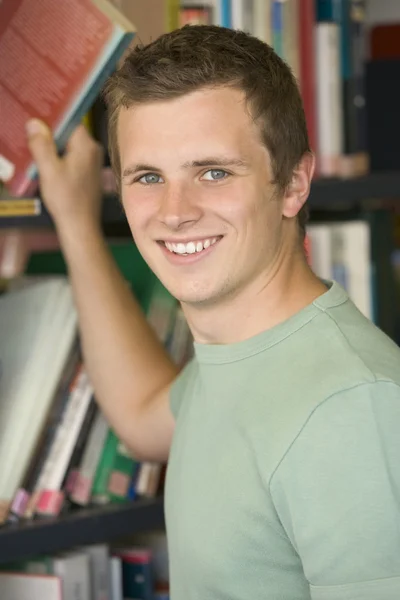 Male college student reaching for a library book — Stock Photo, Image