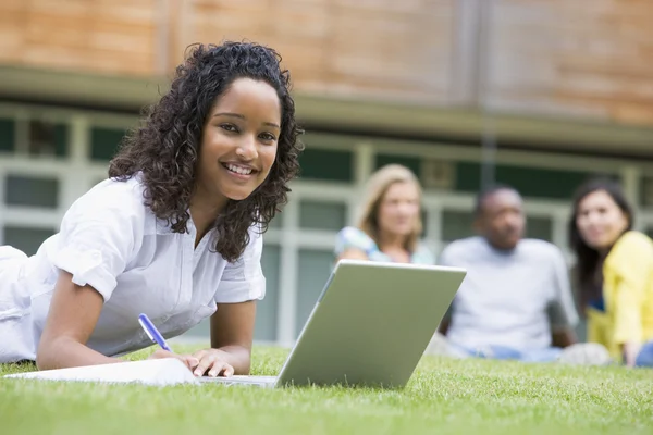 Młoda kobieta korzysta z laptopa na trawniku kampusu, z innych studentów rel — Zdjęcie stockowe
