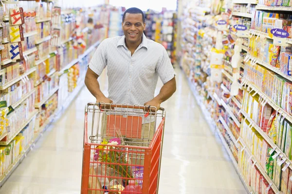 Człowiek pchanie wózka wzdłuż nawy supermarketu — Zdjęcie stockowe