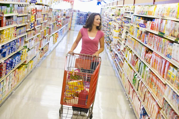 Woman pushing trolley along supermarket aisle — Stock Photo, Image