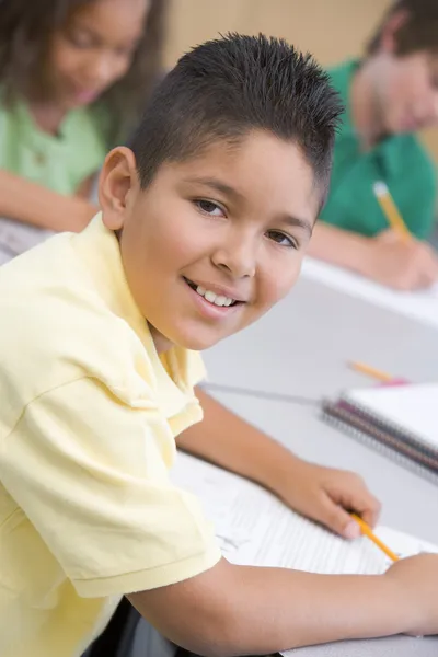 小学校教室の机で書くの男子生徒 — ストック写真