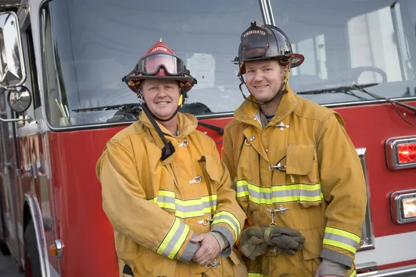 Portrait of two firefighters by a fire engine — Stock Photo, Image