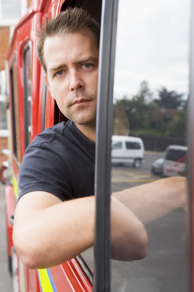 Férfi tűzoltó ül a vezetőfülkében egy tűzoltóautó — Stock Fotó