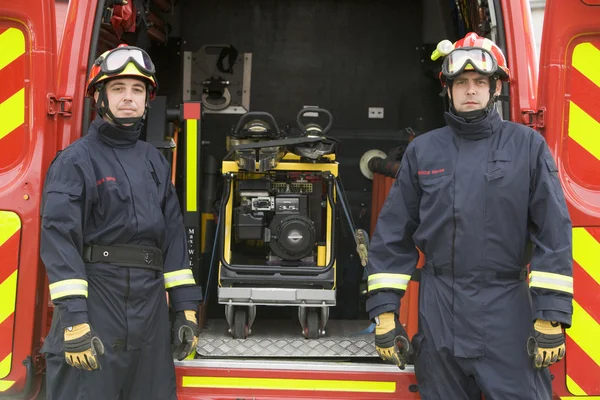 Пожежники, що стоять біля обладнання у маленькому пожежному двигуні — стокове фото