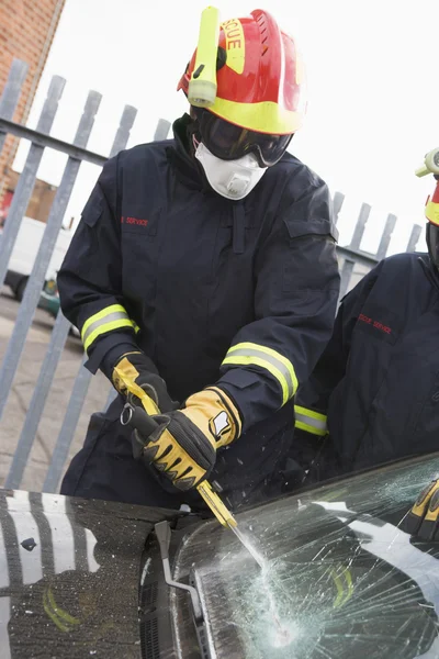 Firefighters breaking a car windscreen to help a car crash victi — Stock Photo, Image