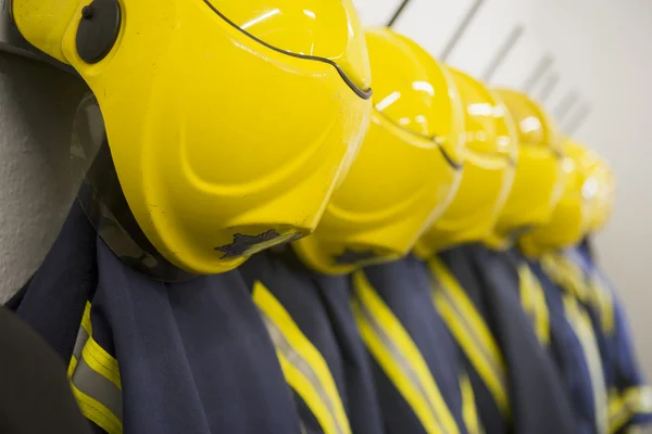Casacos e capacetes de bombeiro pendurados num quartel de bombeiros — Fotografia de Stock