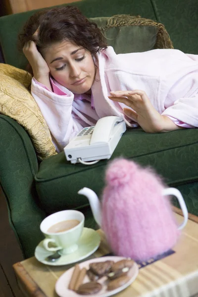 Eine junge Frau liegt auf ihrer Couch und schaut dem Telefon zu — Stockfoto