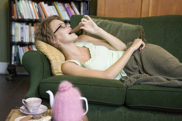 Uma jovem deitada em seu sofá comendo chocolate — Fotografia de Stock