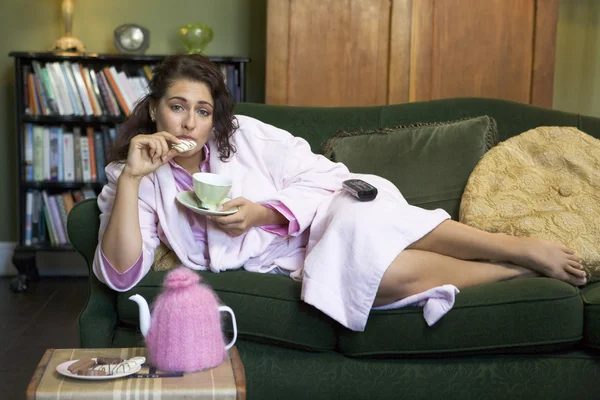 Una giovane donna sdraiata sul suo divano a bere tè — Foto Stock