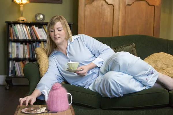 Молодая женщина лежит на диване и пьет чай. — стоковое фото