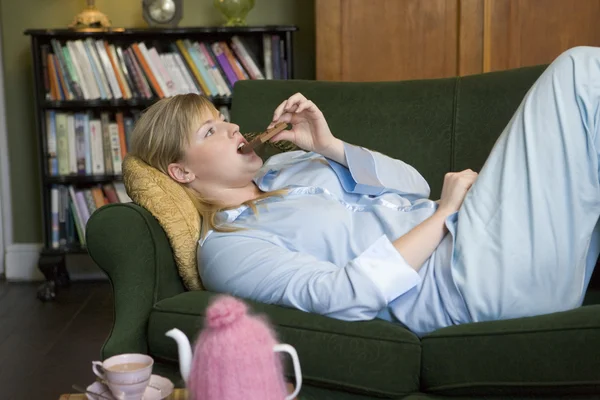 En ung kvinna liggande på hennes soffa äta choklad — Stockfoto