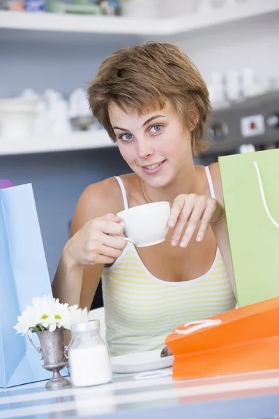 一个年轻女子坐在咖啡厅与喝茶的购物袋 — 图库照片