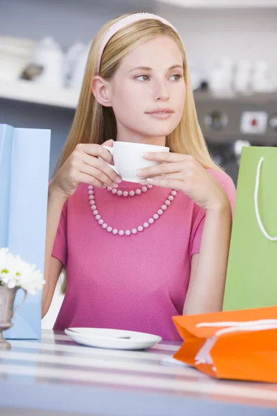 Μια νεαρή γυναίκα που κάθεται σε ένα καφέ με τσάντες αγορών πίνοντας τσάι — Φωτογραφία Αρχείου