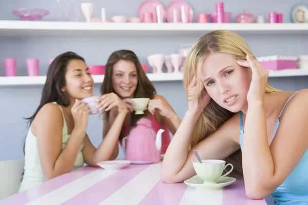 两个年轻妇女享受茶党 而一个分开坐 — 图库照片