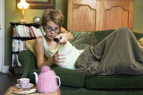 Une jeune femme allongée sur son canapé regardant la télévision — Photo
