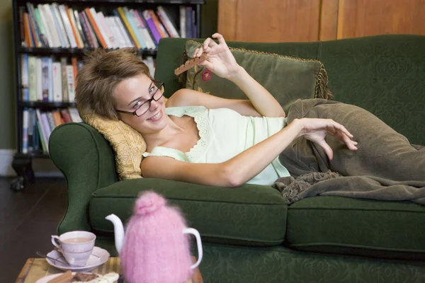 Молодая женщина лежит на диване и ест шоколад. — стоковое фото