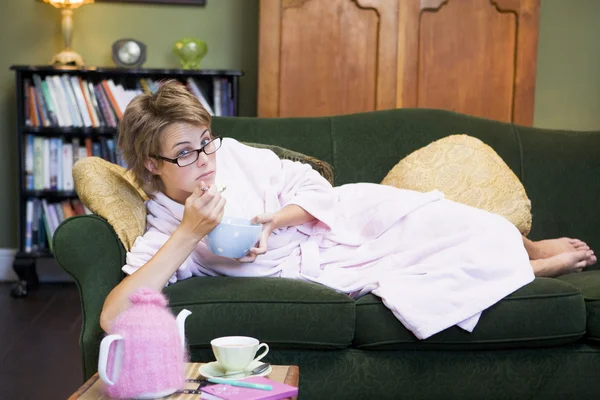 Eine junge Frau liegt auf ihrer Couch und isst Müsli — Stockfoto