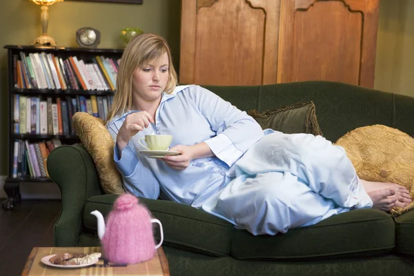 お茶を飲む彼女のソファに横になっている若い女性 — ストック写真
