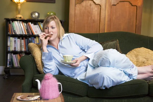 Eine junge Frau liegt auf ihrem Sofa und trinkt Tee — Stockfoto
