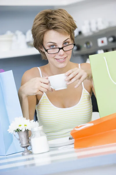 Mladá žena sedí v kavárně s nákupní tašky pití čaje — Stock fotografie