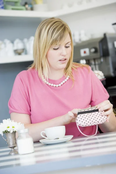 A young woman sitting in a cafe looking worried into her purse — Stock Photo, Image