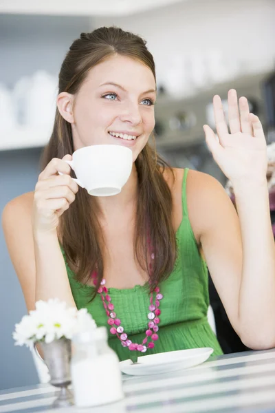 Молодая женщина сидит в кафе, пьет чай и машет рукой. — стоковое фото