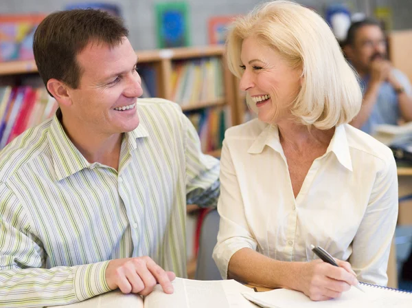 Reife Studentin lacht mit Nachhilfelehrer in Bibliothek — Stockfoto