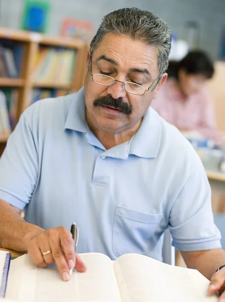 Зрелый студент-мужчина учится в библиотеке — стоковое фото