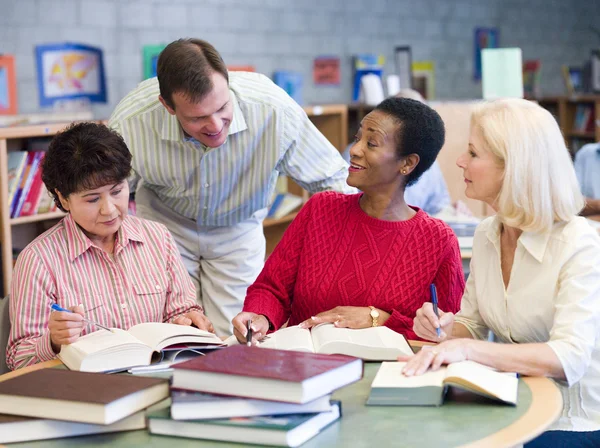 Teacher helping mature students in library — Stock Photo, Image