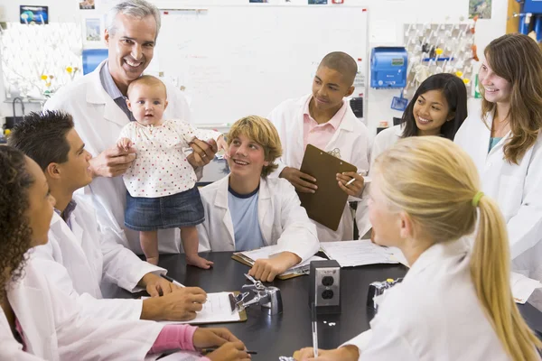 Ein naturwissenschaftlicher Lehrer mit einem Baby umgeben von Schülern in einer High-Tech-Schule — Stockfoto