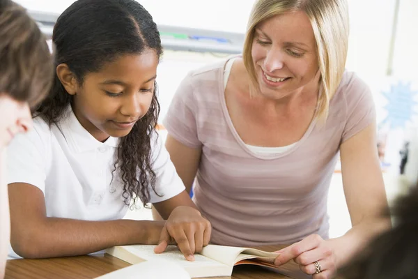 Una colegiala y su maestra leyendo un libro en clase — Foto de Stock