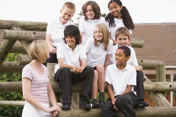 Schulkinder sitzen draußen mit ihrem Lehrer auf Bänken — Stockfoto