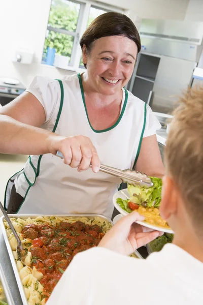 Lunchlady serving plate of lunch in school cafeteria — Stock Photo, Image