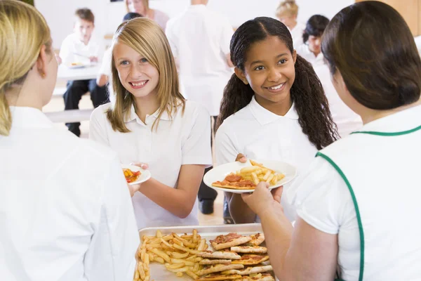 Lunchladies serving plates of lunch in school cafeteria — Stock Photo, Image