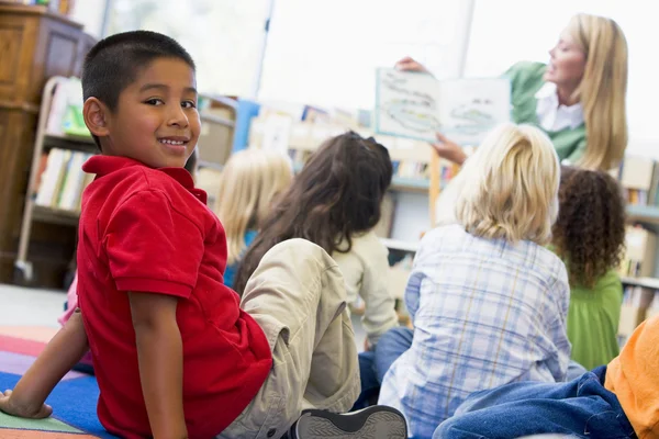 Nauczyciel przedszkola czytania dzieciom w bibliotece, chłopak szuka — Zdjęcie stockowe